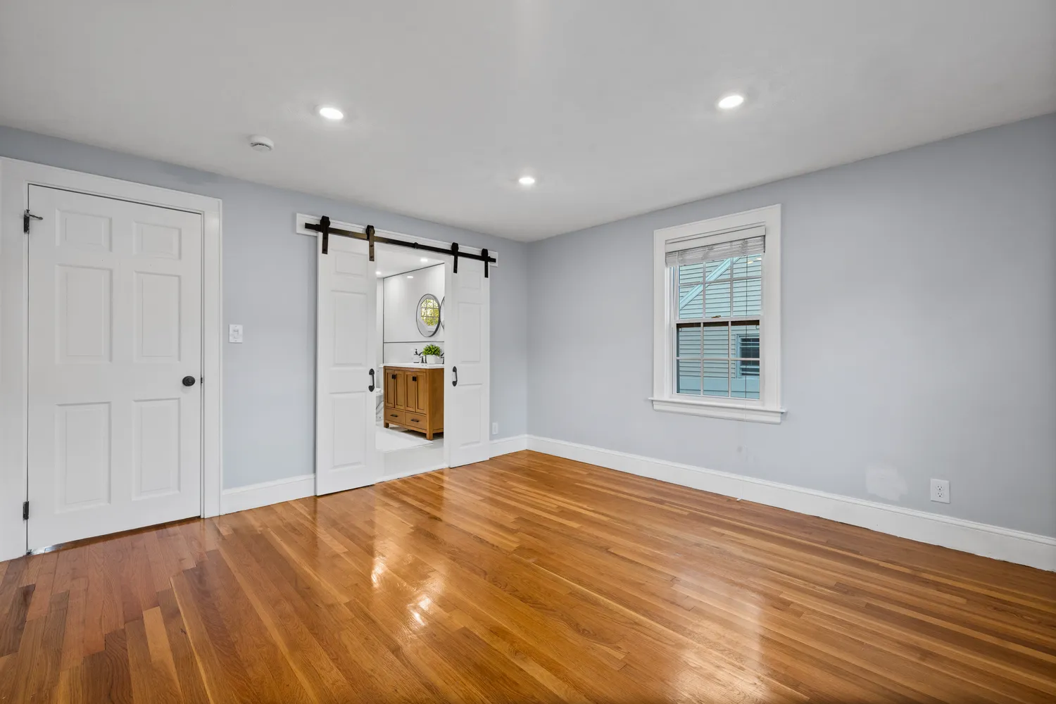 a view of an empty room with wooden floor and window