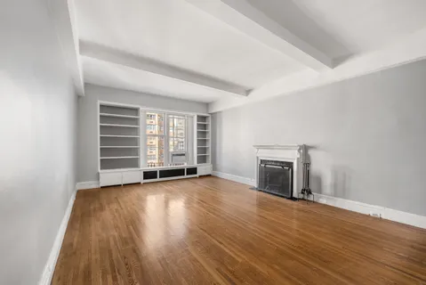 an empty room with wooden floor fireplace and windows