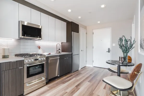a kitchen with stainless steel appliances a stove a microwave a sink white cabinets and wooden floor