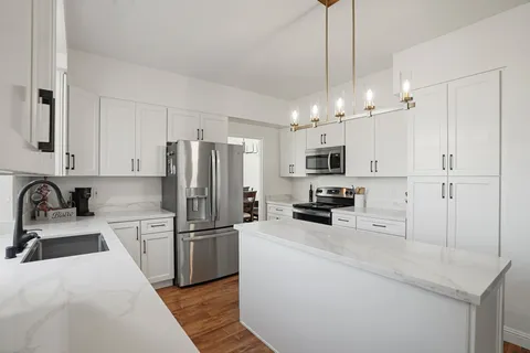 a kitchen with granite countertop a refrigerator a sink and white cabinets