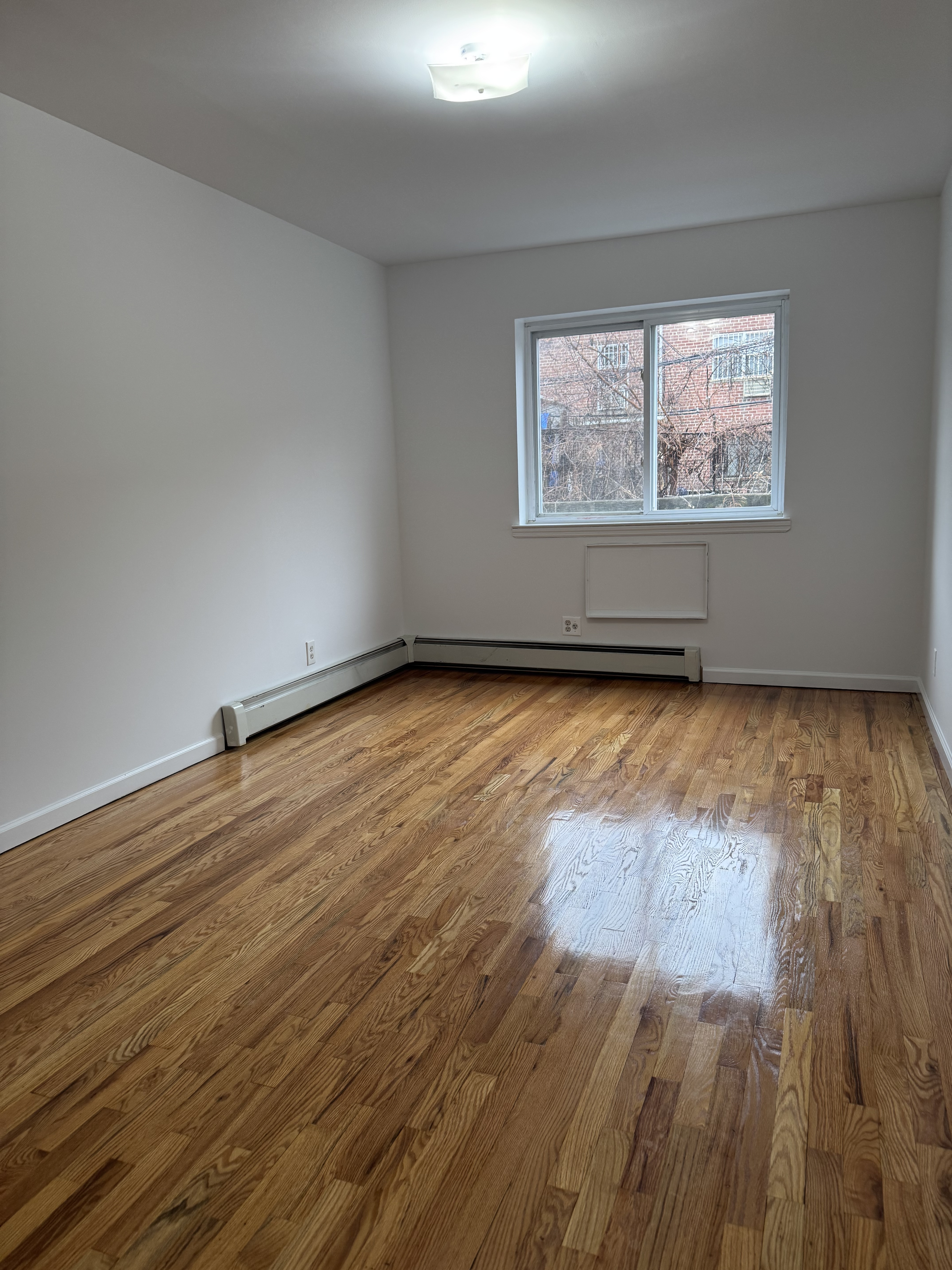 39-46 59th Street, Unit 1 Queens, NY 11377 - Photo 2 of 6 wooden floor in an empty room with a window
