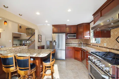 a kitchen with stainless steel appliances granite countertop a stove top oven a sink dishwasher and a refrigerator with wooden cabinets