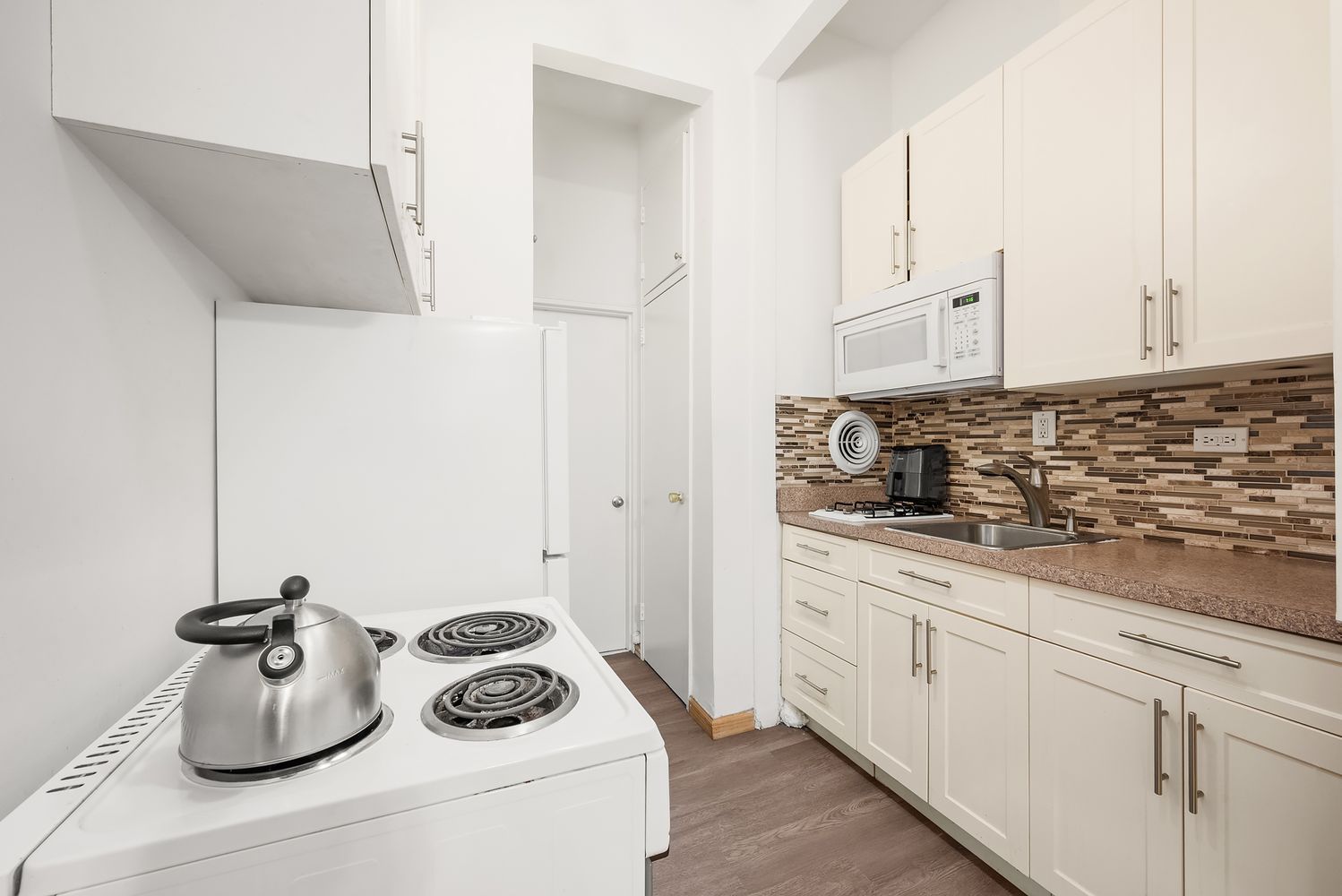 430 East 85th Street, Unit 1B Manhattan, NY 10028 - Photo 4 of 8 a kitchen with a sink a stove and white cabinets