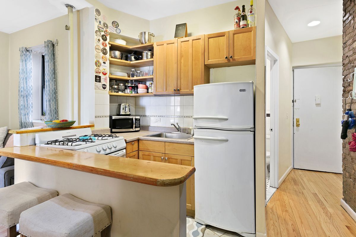 309 East 95th Street, Unit 27 Manhattan, NY 10128 - Photo 3 of 8 a kitchen with a refrigerator a stove a sink and a dining table with wooden floor