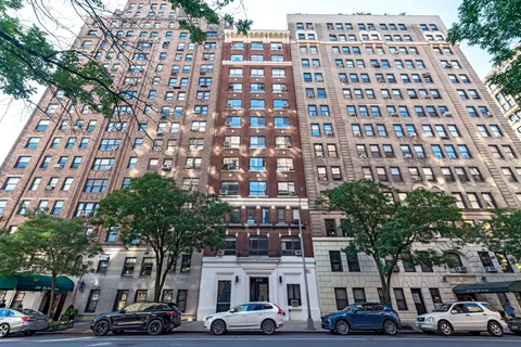 a front view of a building with lot of cars and trees