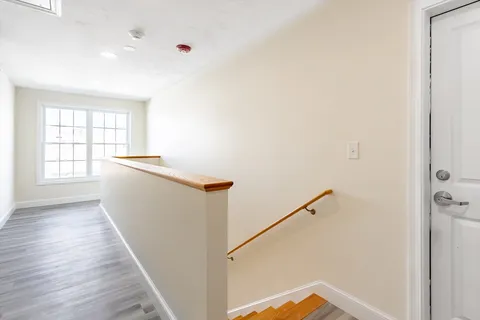 a view of hallway with window and wooden floor