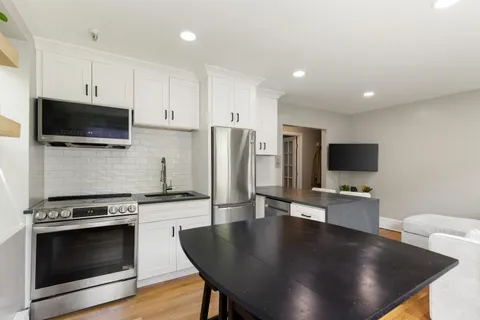 a living room with stainless steel appliances a fireplace a flat screen tv and view kitchen