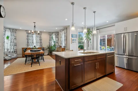 a kitchen with stainless steel appliances granite countertop a refrigerator a sink dishwasher a dining table and chairs with wooden floor