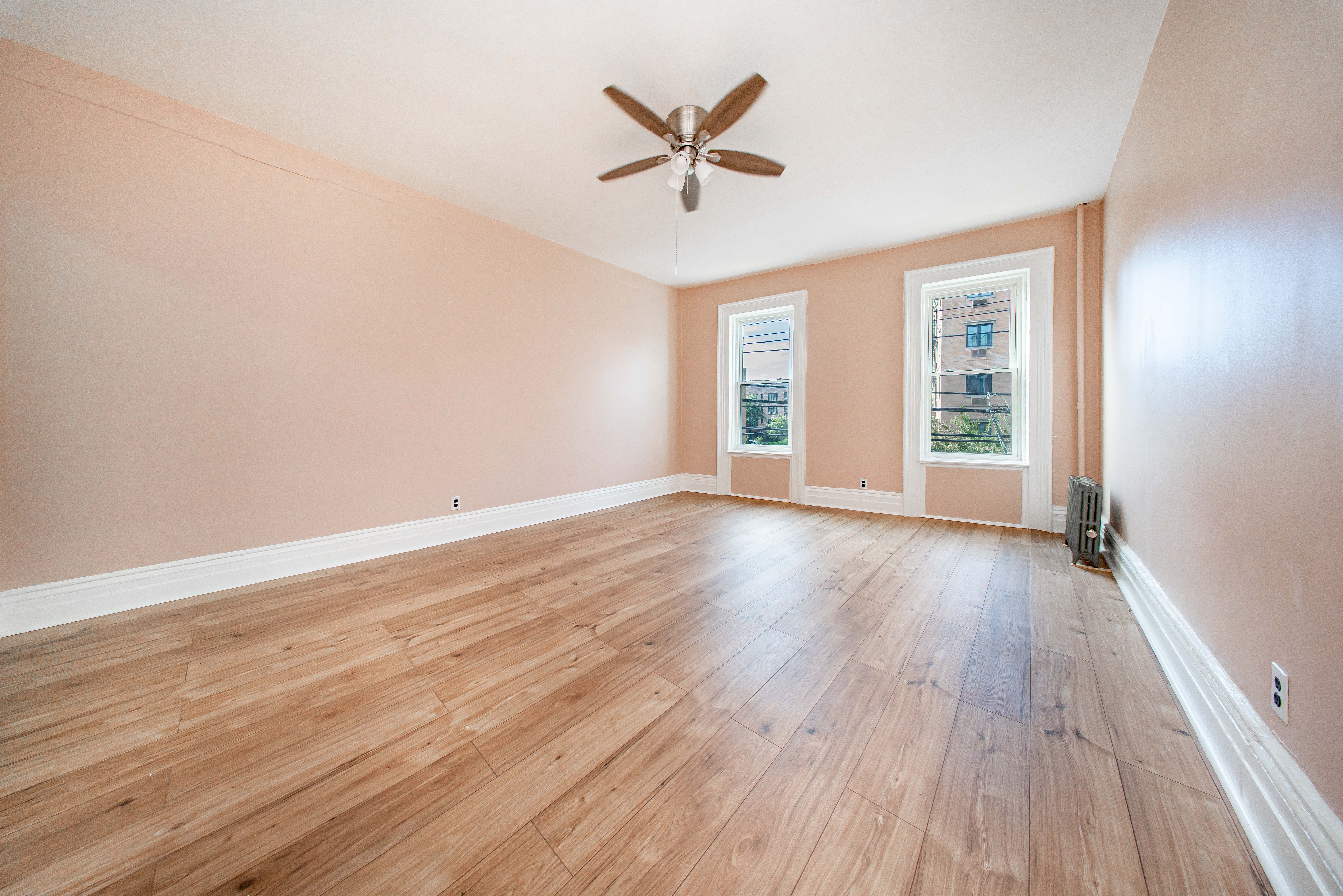 22-17 Astoria Boulevard, Unit 2W Queens, NY 11102 - Photo 3 of 10 an empty room with wooden floor chandelier fan and windows