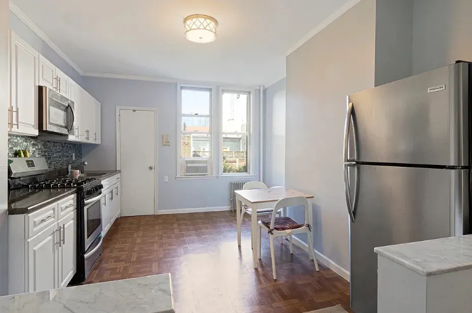 a kitchen with granite countertop a refrigerator a sink dishwasher a stove top oven a dining table and chairs with wooden floor