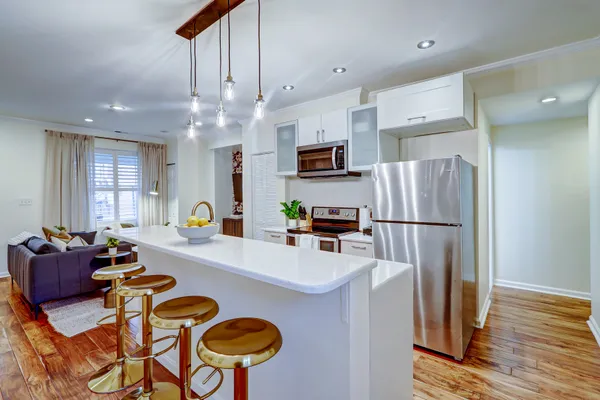 a kitchen with stainless steel appliances granite countertop a refrigerator a sink dishwasher a stove a dining table and chairs with wooden floor