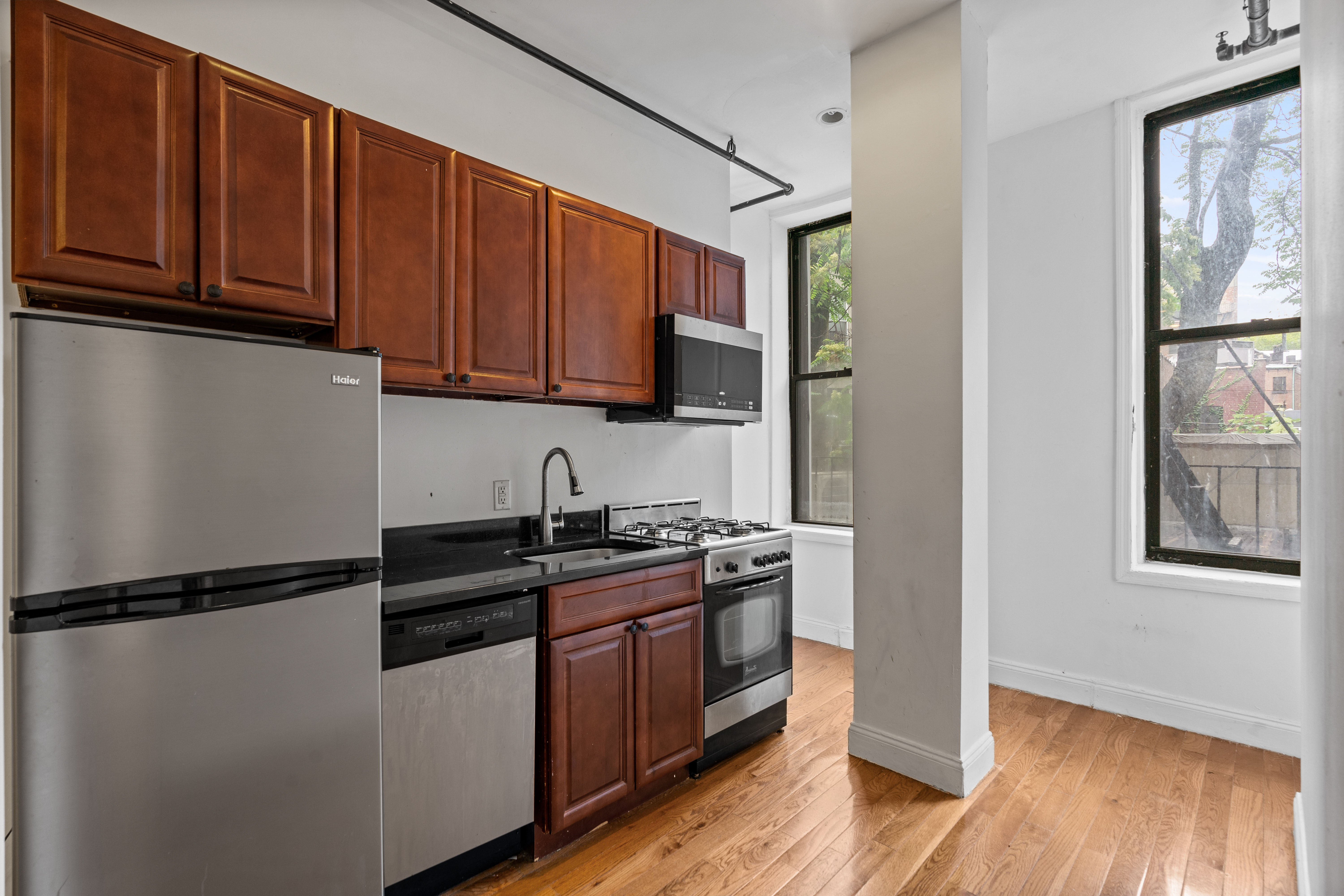 31 St Marks Place, Unit 1 Manhattan, NY 10003 - Photo 7 of 11 a kitchen with stainless steel appliances granite countertop a refrigerator a sink dishwasher and wooden cabinets with wooden floor