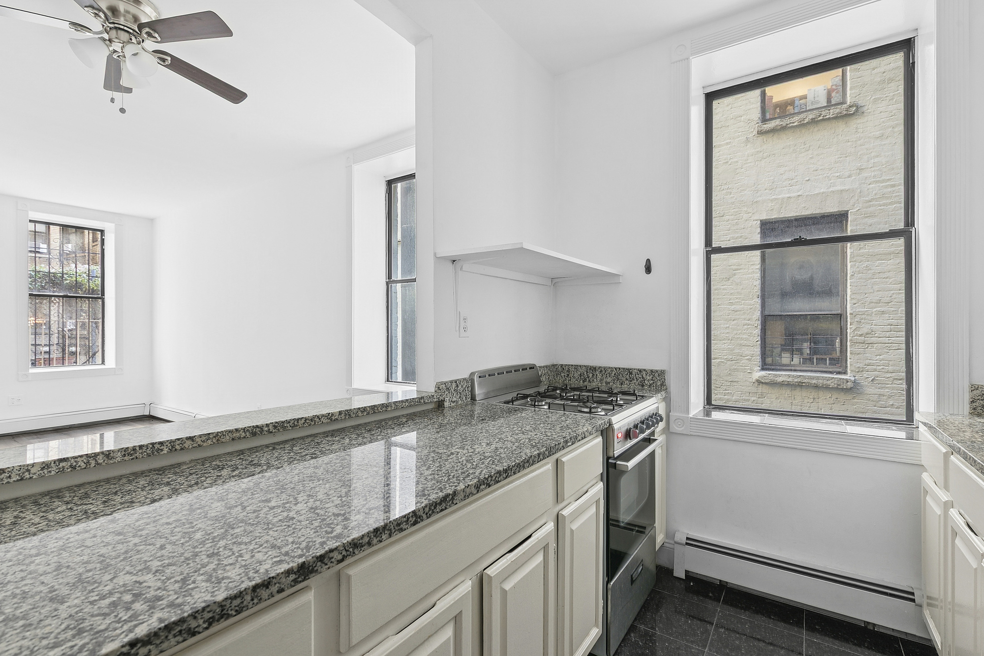 178 East 2nd Street, Unit 1B Manhattan, NY 10009 - Photo 6 of 11 a kitchen with granite countertop a sink stainless steel appliances white cabinets and a window