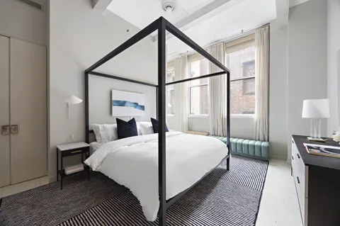 a bedroom with a bed table and two large window