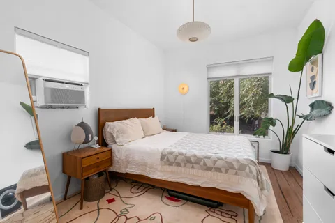 a bedroom with a bed table flowerpot and window