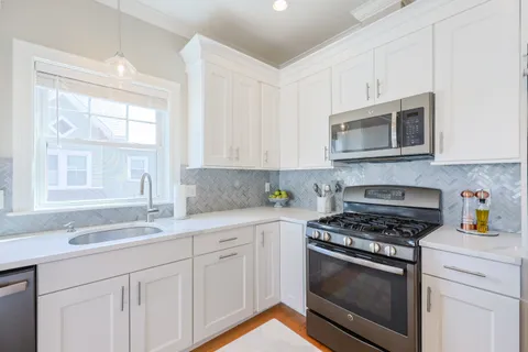 a kitchen with granite countertop white cabinets stainless steel appliances and a window