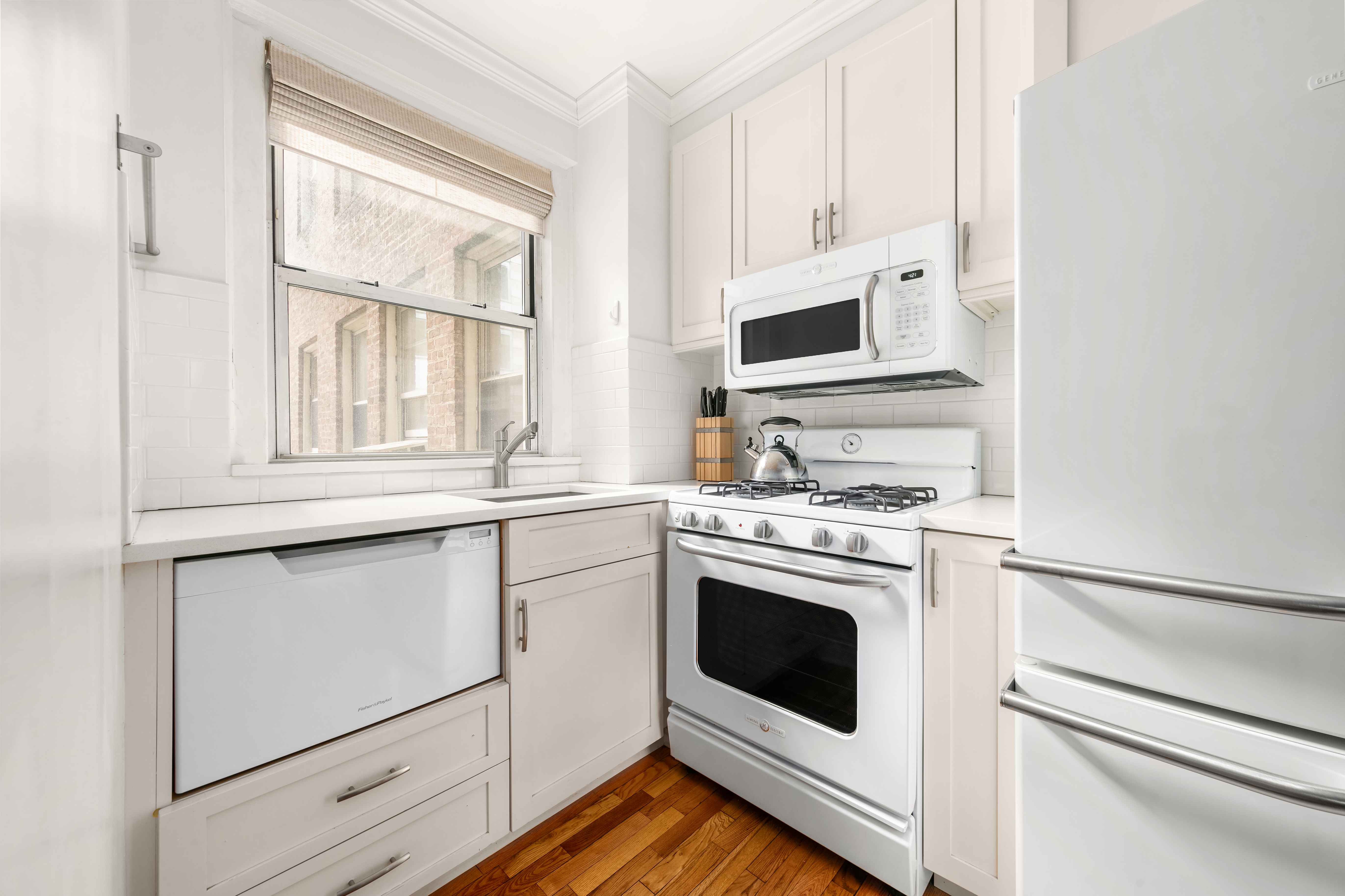 333 East 43rd Street, Unit 311 Manhattan, NY 10017 - Photo 5 of 18 a kitchen with granite countertop white cabinets appliances and a window