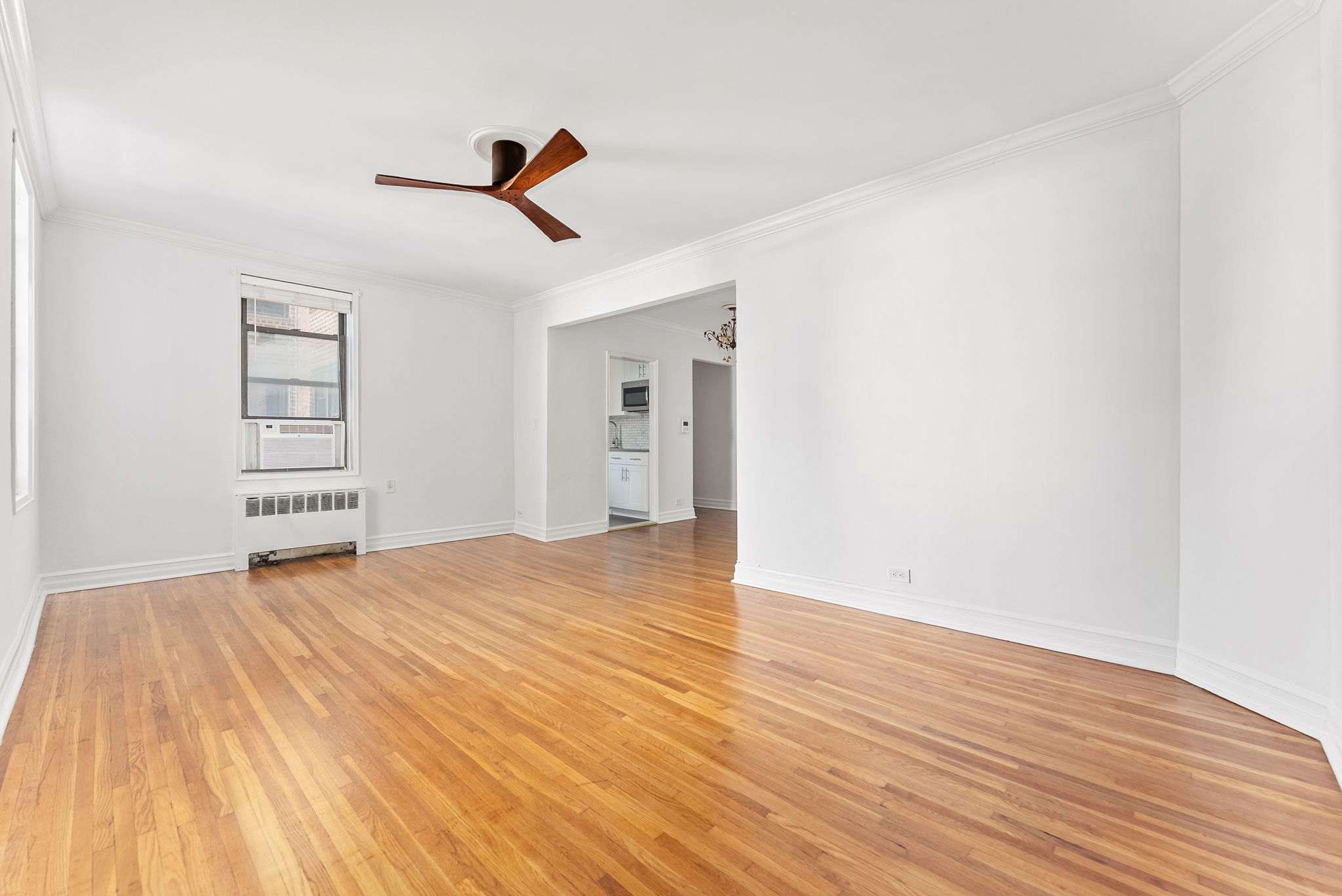675 Academy Street, Unit 3A Manhattan, NY 10034 - Photo 3 of 12 an empty room with wooden floor ceiling fan and windows