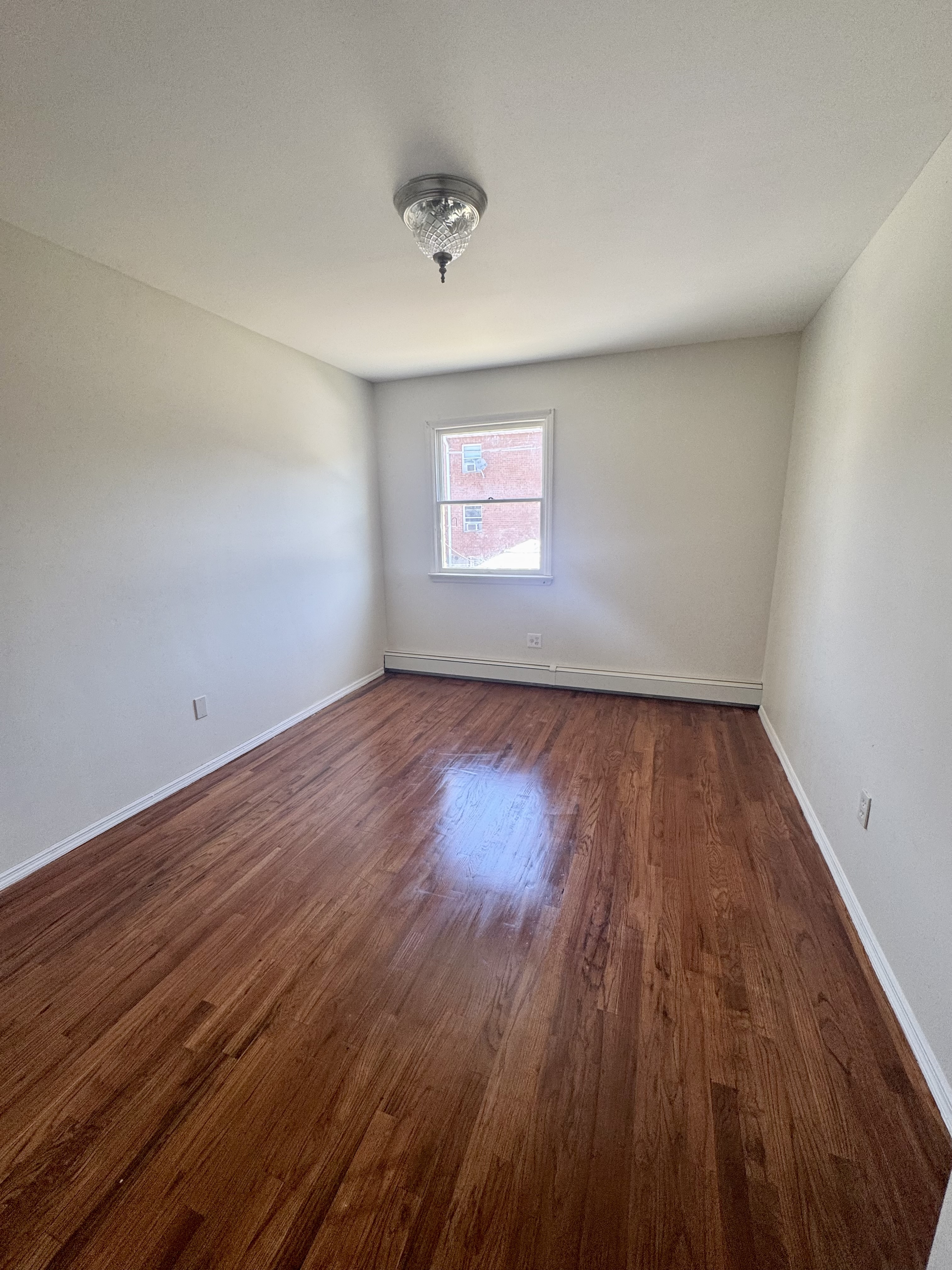 156-17 76th Street, Unit 1 Queens, NY 11414 - Photo 5 of 12 an empty room with wooden floor and windows