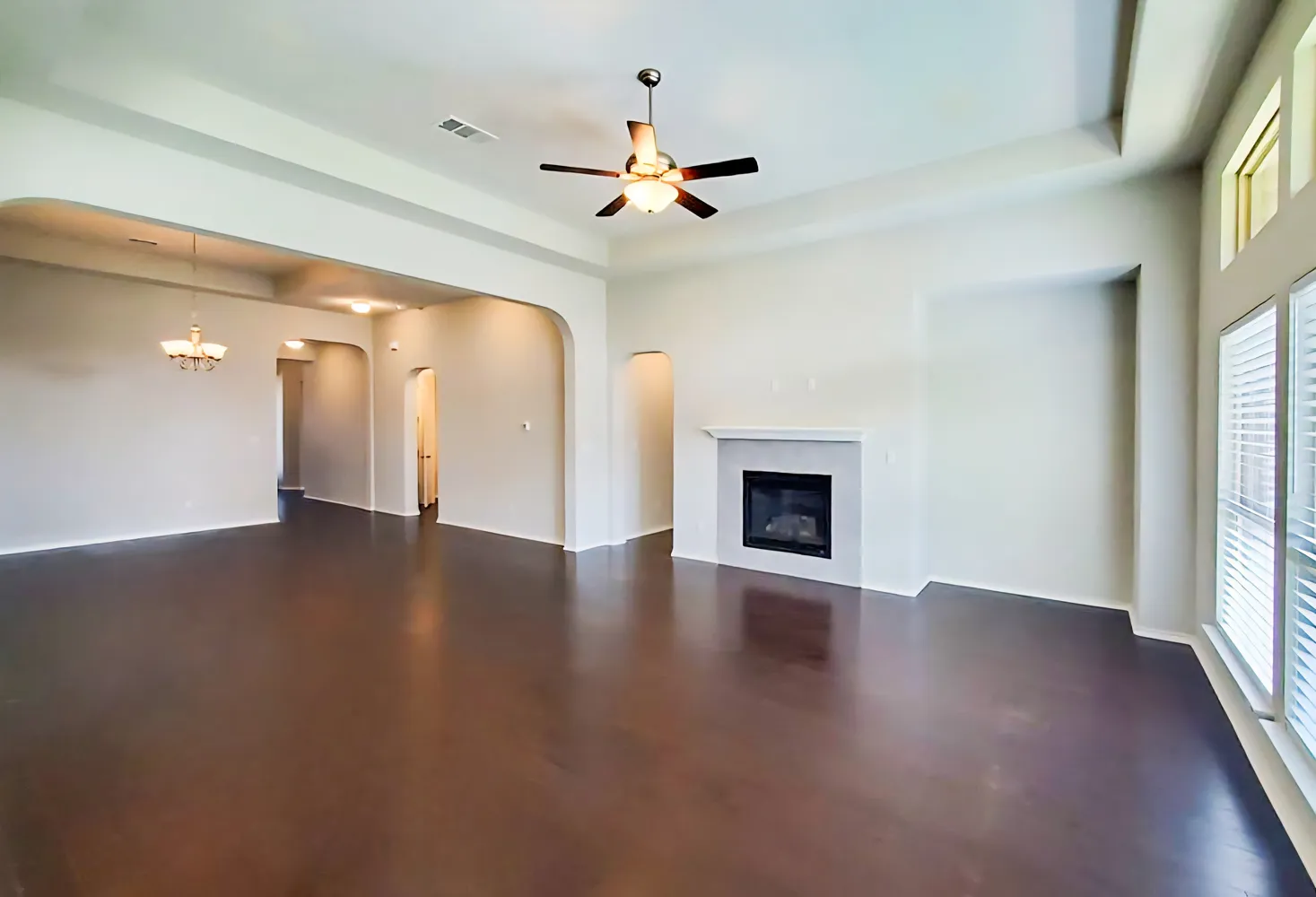 an empty room with wooden floor chandelier fan and windows