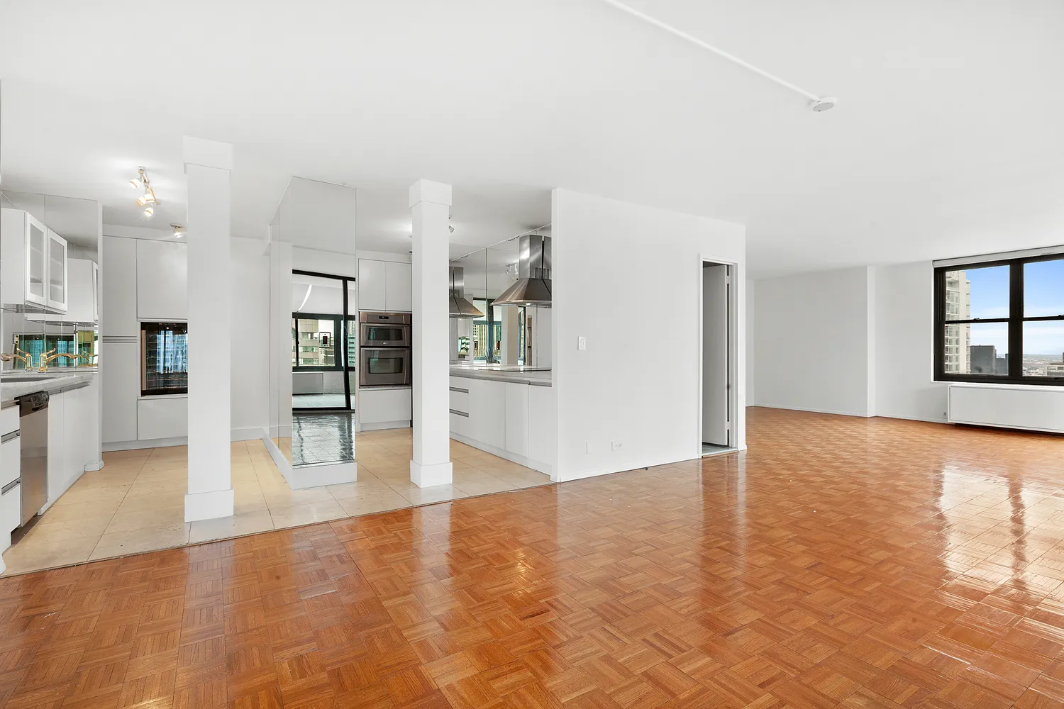 a view of an empty room with kitchen and window