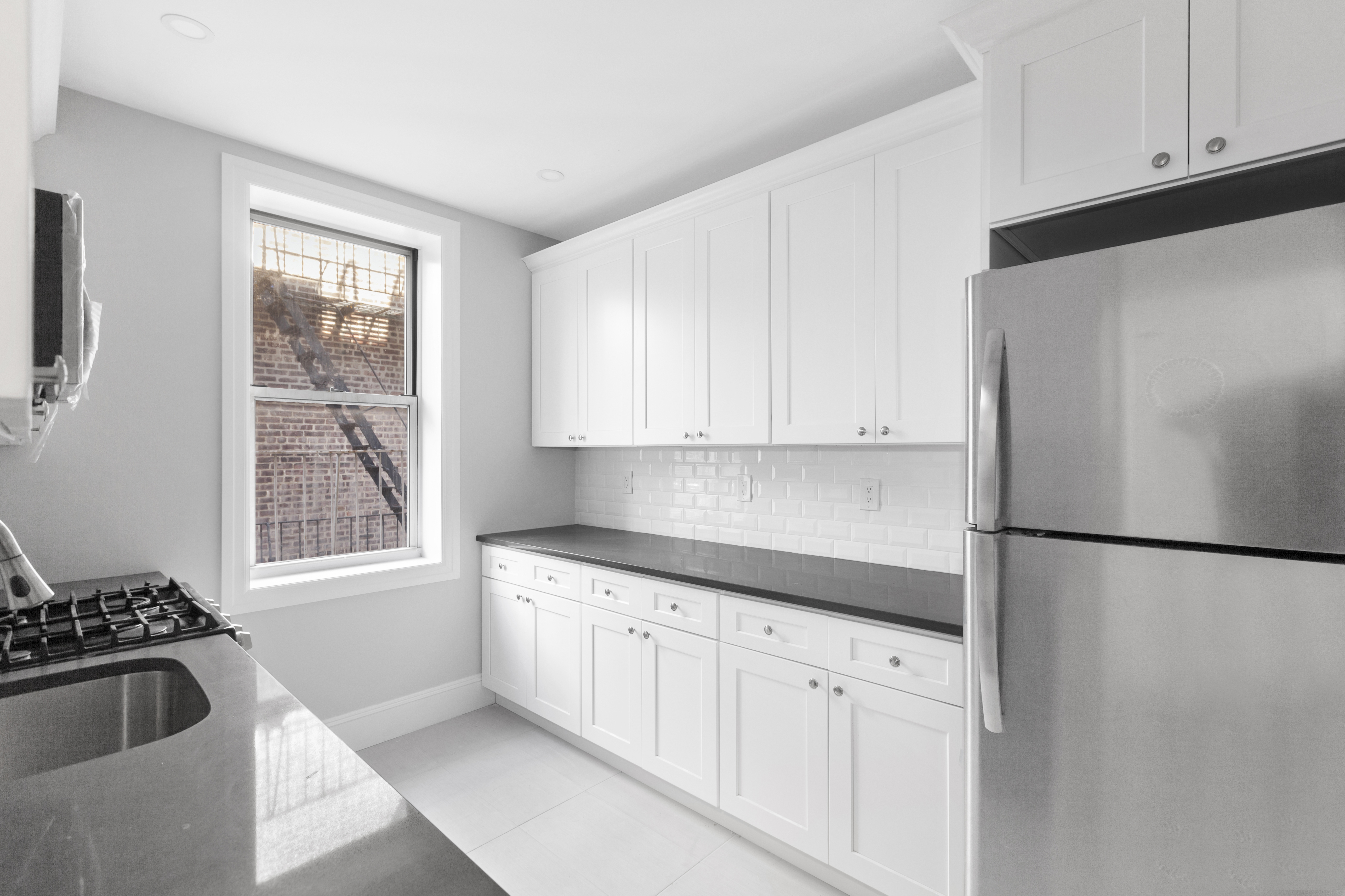 45-15 41st Street, Unit 3R Queens, NY 11104 - Photo 2 of 7 a kitchen with granite countertop white cabinets and refrigerator