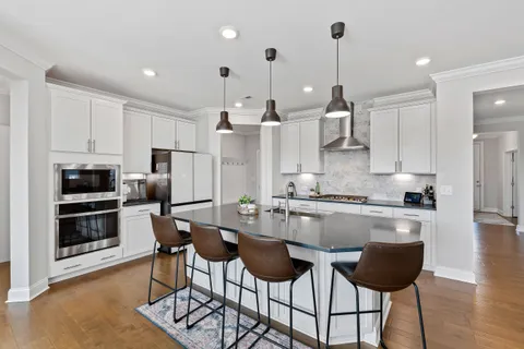 a kitchen with stainless steel appliances granite countertop a stove top oven a refrigerator a sink and chairs