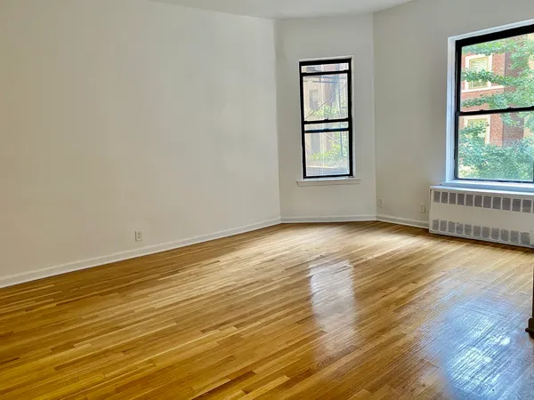 a view of an empty room with wooden floor and windows