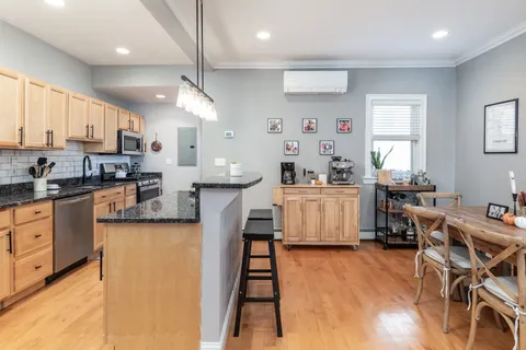 a kitchen with stainless steel appliances kitchen island granite countertop a refrigerator a stove a sink dishwasher and white cabinets with wooden floor next to windows