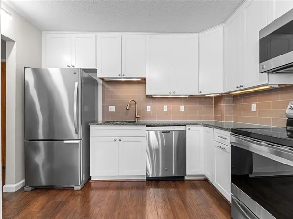 a kitchen with granite countertop a refrigerator stove and white cabinets