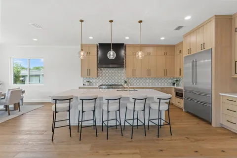 a kitchen with stainless steel appliances granite countertop a kitchen island a stove a refrigerator a sink a dining table and chairs with wooden floor