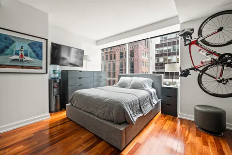 a bedroom with a bed a flat screen tv and dresser next to a window