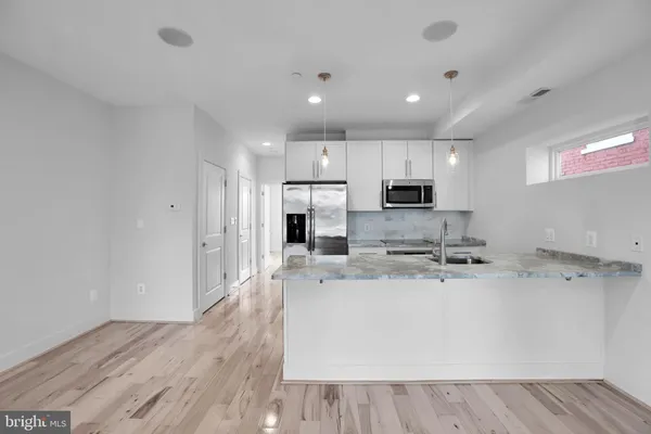 a large kitchen with stainless steel appliances granite countertop a stove a sink a refrigerator and white cabinets with wooden floor