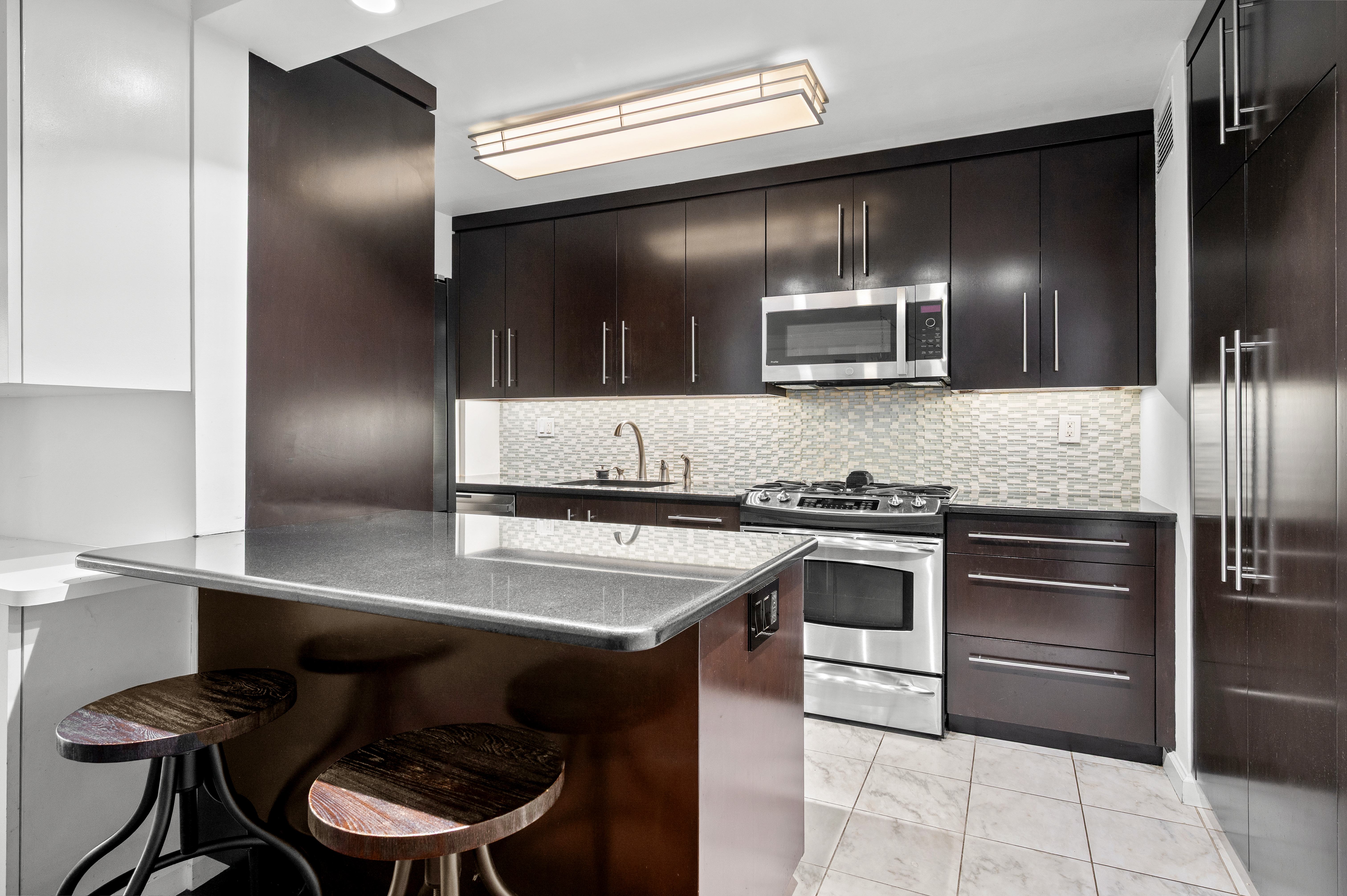225 East 57th Street, Unit 14F Manhattan, NY 10022 - Photo 5 of 14 a kitchen with kitchen island stainless steel appliances and chairs