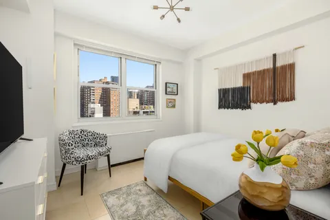 a bedroom with a bed a couch and a potted plant on the dresser
