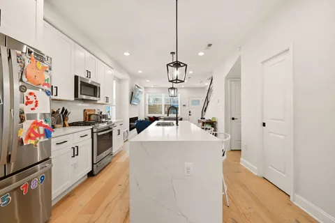 a white kitchen with stainless steel appliances granite countertop a sink dishwasher a refrigerator and a stove with wooden floor