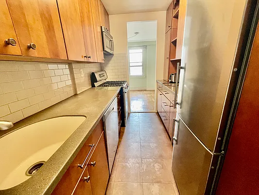 900 West 190th Street, Unit 9B Manhattan, NY 10040 - Photo 8 of 16 a view of a kitchen with kitchen island a sink a refrigerator and a window