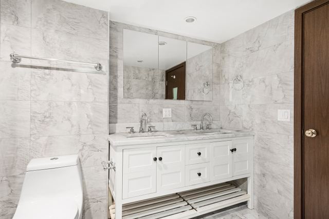 1773 1st Avenue, Unit 1 Manhattan, NY 10128 - Photo 4 of 8 a bathroom with a granite countertop sink a toilet a mirror and shower