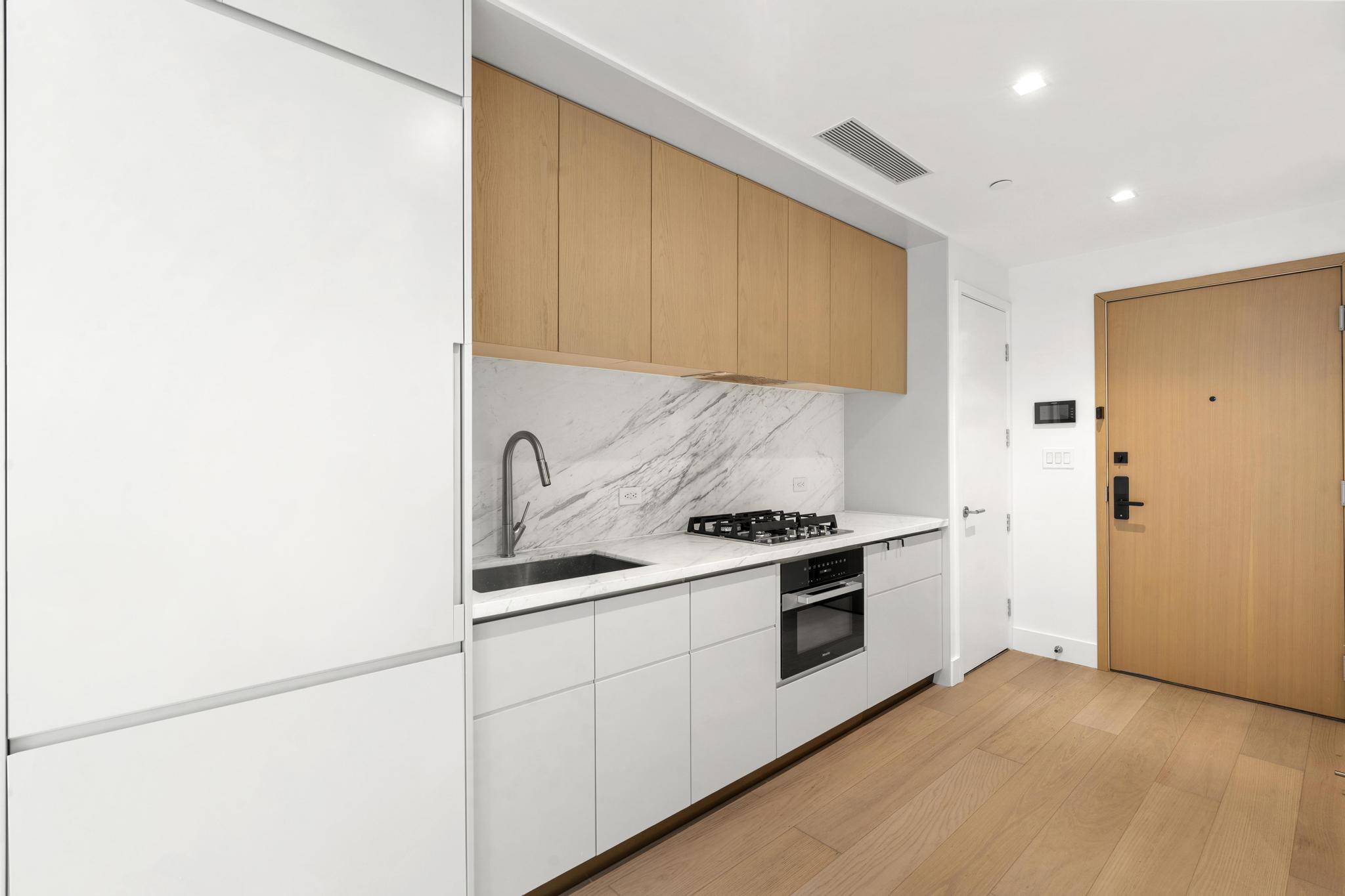 208 Delancey Street, Unit GC Manhattan, NY 10002 - Photo 4 of 12 a kitchen with granite countertop white cabinets and stainless steel appliances