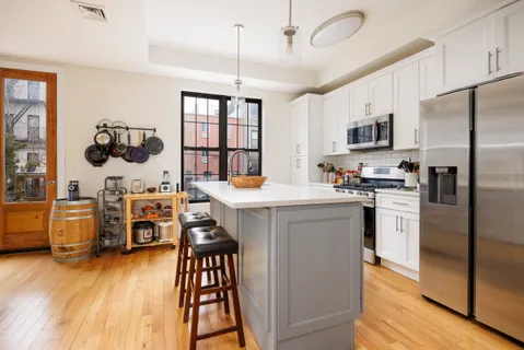 a kitchen with stainless steel appliances kitchen island granite countertop a refrigerator a stove a sink dishwasher a dining table and chairs with wooden floor