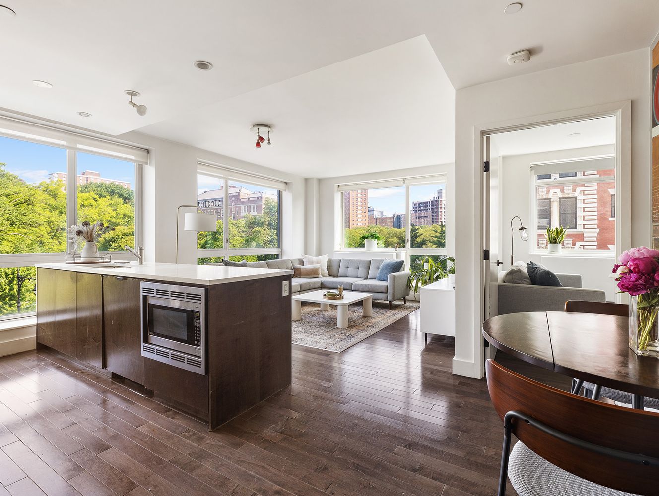 a living room with stainless steel appliances furniture large windows and wooden floor
