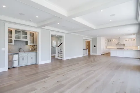 a view of empty room with wooden floor and kitchen view