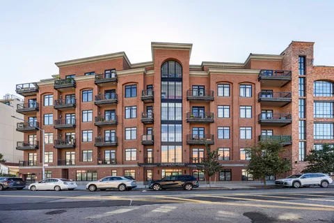 a front view of a building with lot of cars and trees