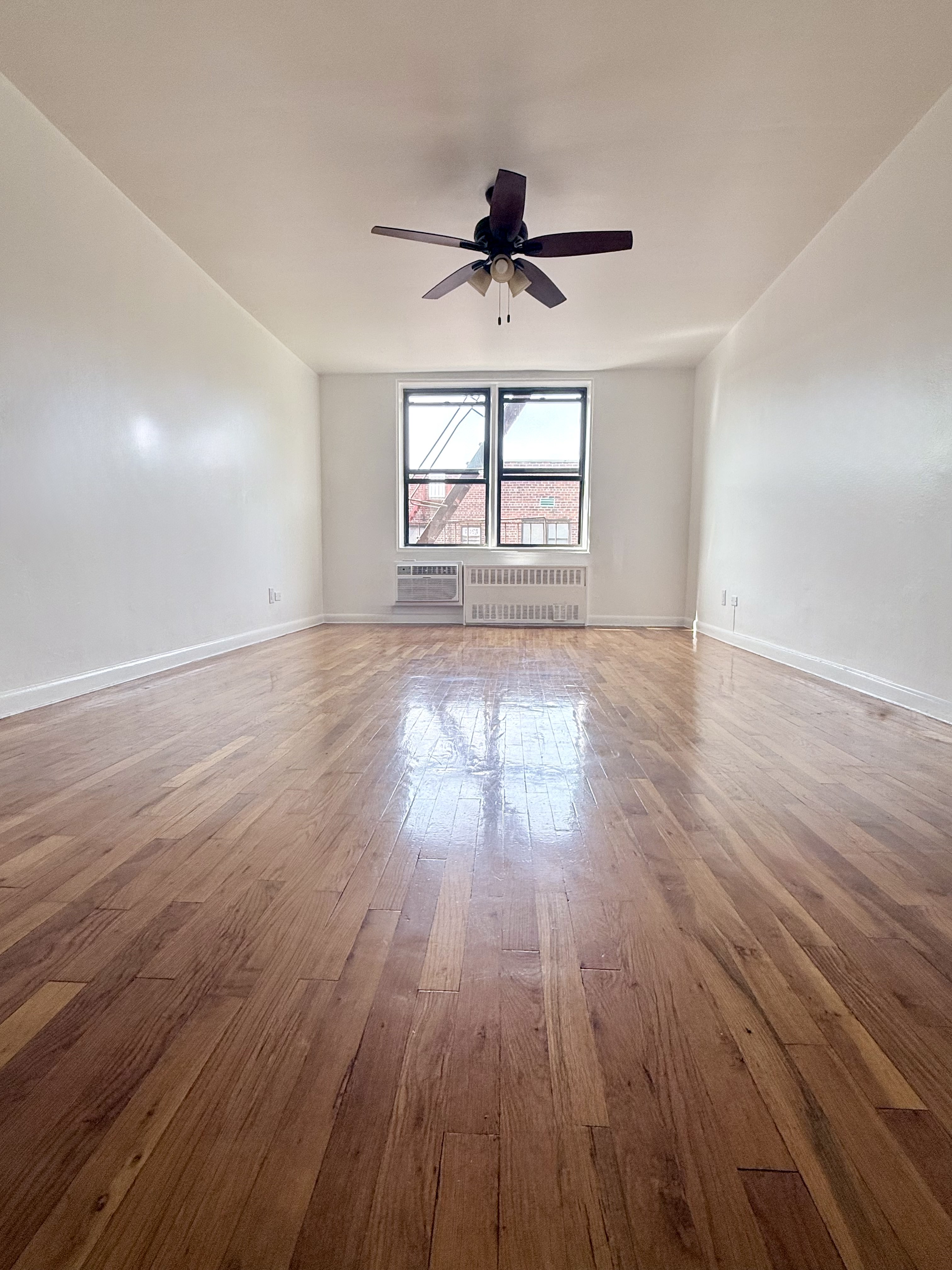 a view of empty room with wooden floor and fan