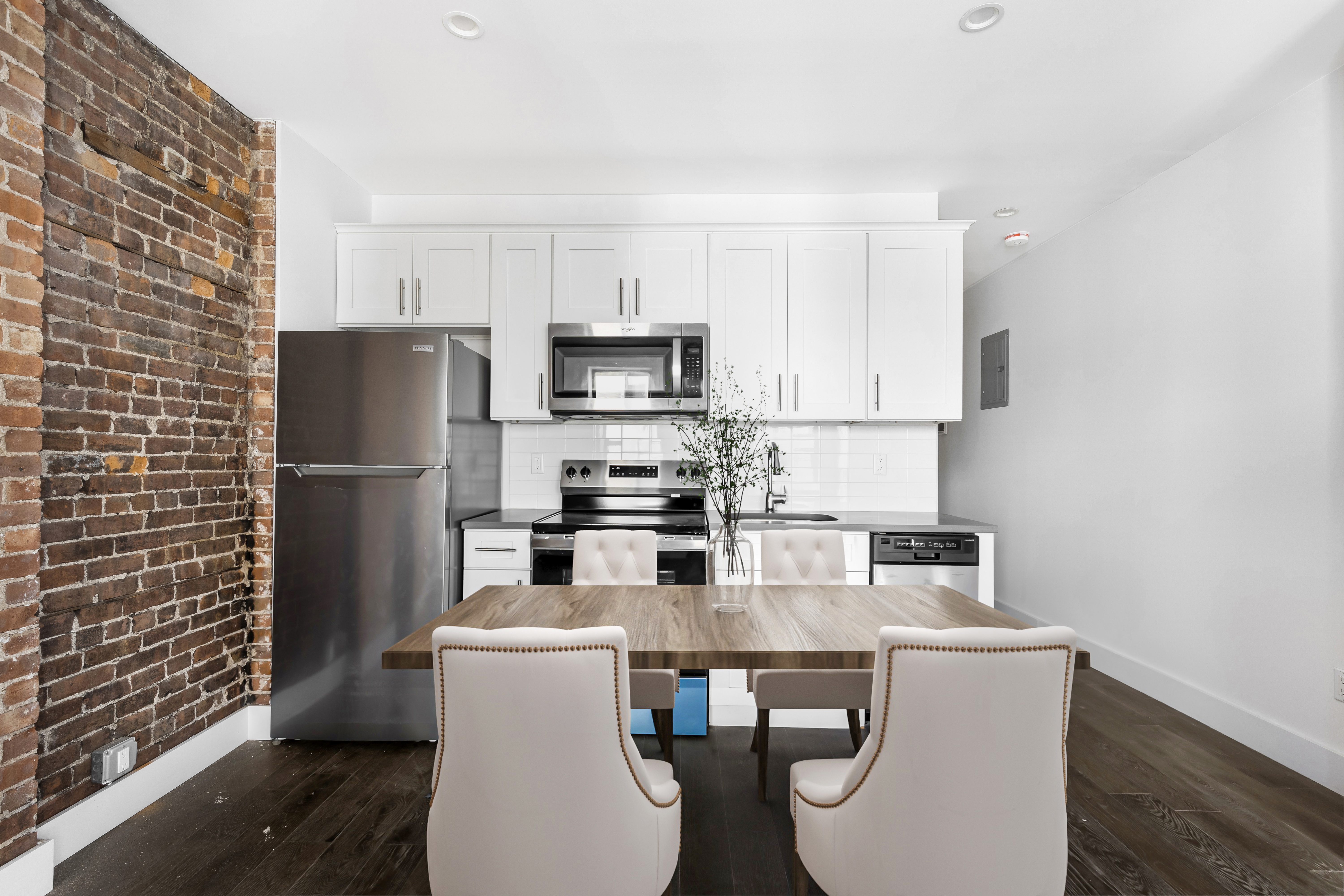 346 West 52nd Street, Unit 5C Manhattan, NY 10019 - Photo 2 of 8 a kitchen with stainless steel appliances a dining table chairs refrigerator and sink