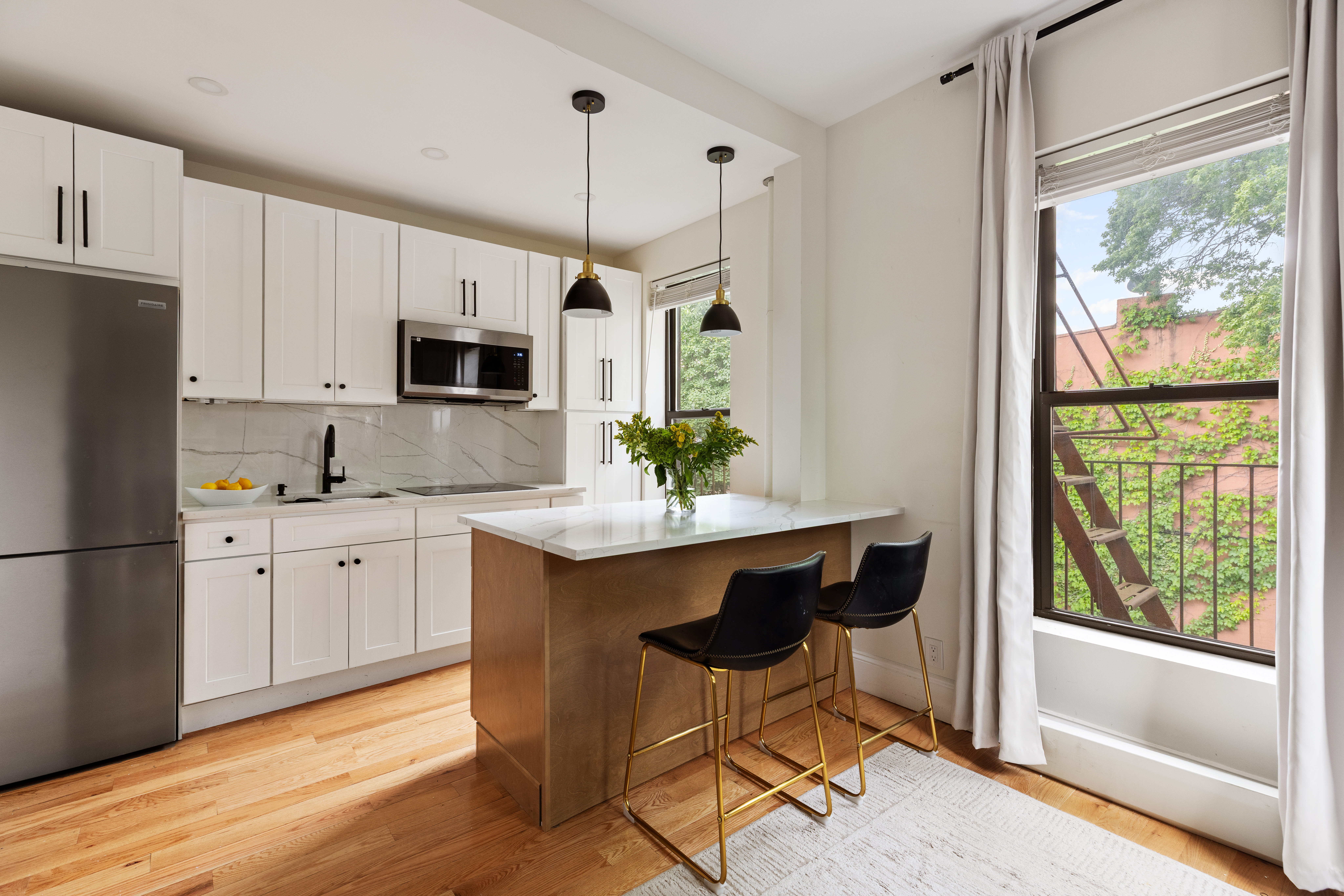 a kitchen with stainless steel appliances granite countertop a stove a sink a microwave a refrigerator and white cabinets with wooden floor