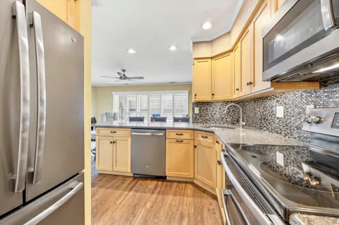 a kitchen with stainless steel appliances granite countertop a refrigerator a sink dishwasher a stove and white countertops with wooden floor