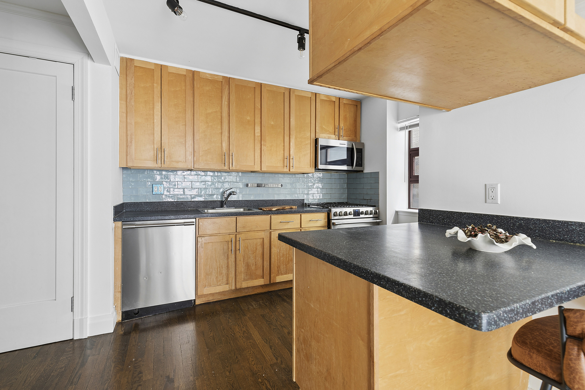 217 East 7th Street, Unit 5CD Manhattan, NY 10009 - Photo 4 of 11 a kitchen with stainless steel appliances granite countertop a sink a stove and white cabinets with wooden floor