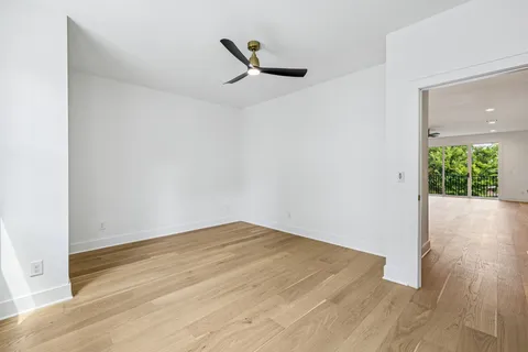 an empty room with wooden floor a ceiling fan and windows