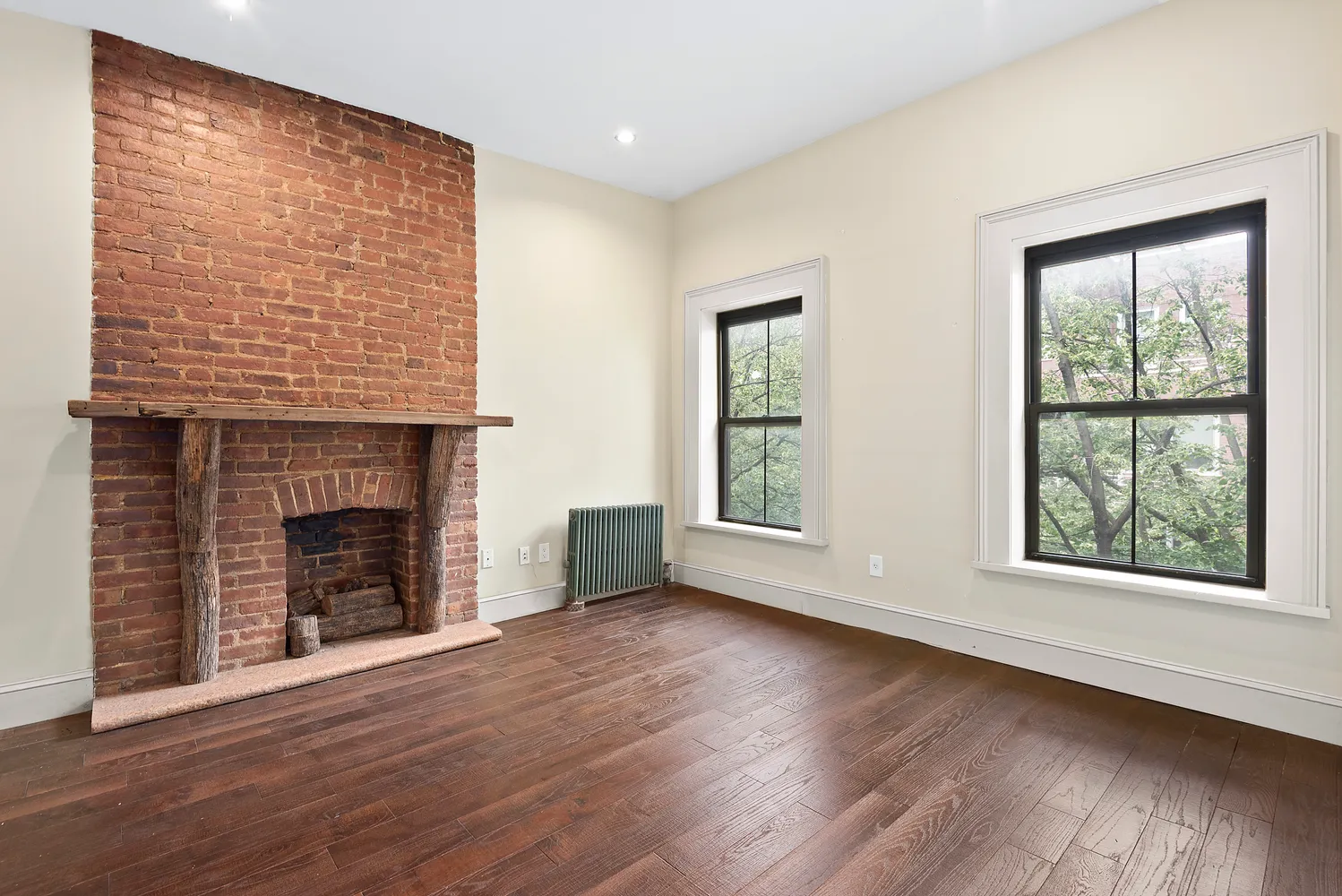 a view of an empty room with wooden floor fireplace and a window